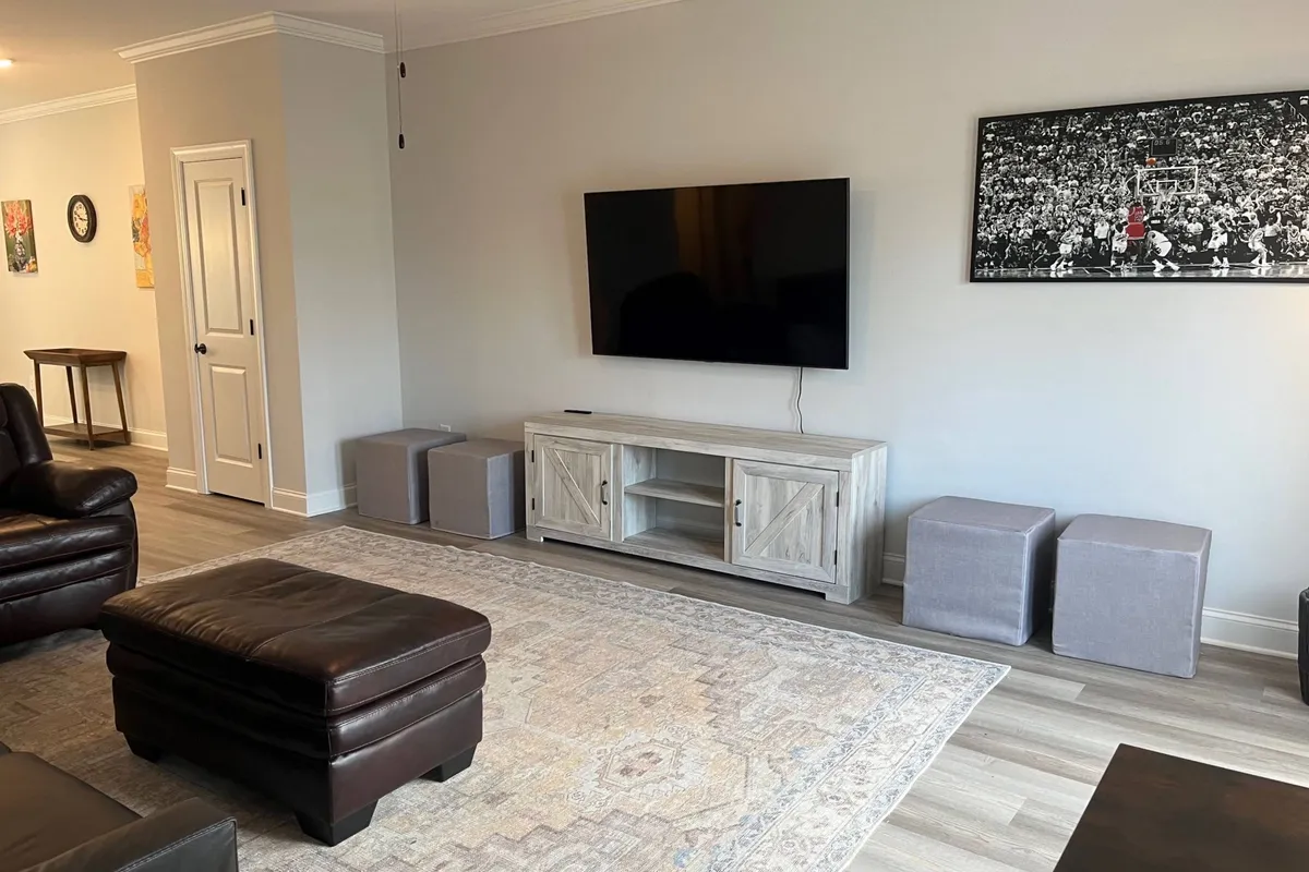A modern, cozy living room with a leather sofa, TV, rug, coffee table, and vibrant artwork. The setup is ideal for unwinding after a long day, whether spent in meetings or virtual calls, and provides a welcoming environment for both work and relaxation.
