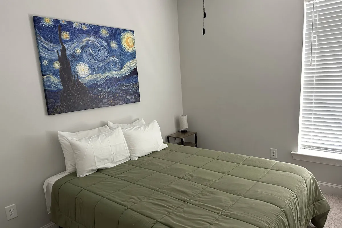 A peaceful bedroom with green bedding, a vibrant wall painting, and a neatly arranged bedside table, evoking a sense of artistic calm and creative relaxation.