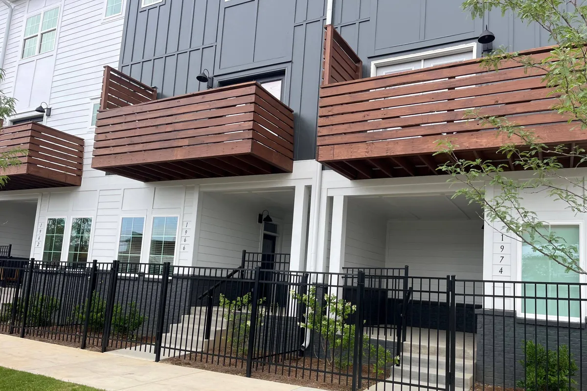 The exterior of Urban Mountain View shows modern wooden balconies and a fenced yard, with inviting areas for relaxing or socializing. The architecture is contemporary, suggesting a comfortable and secure home base within the city.