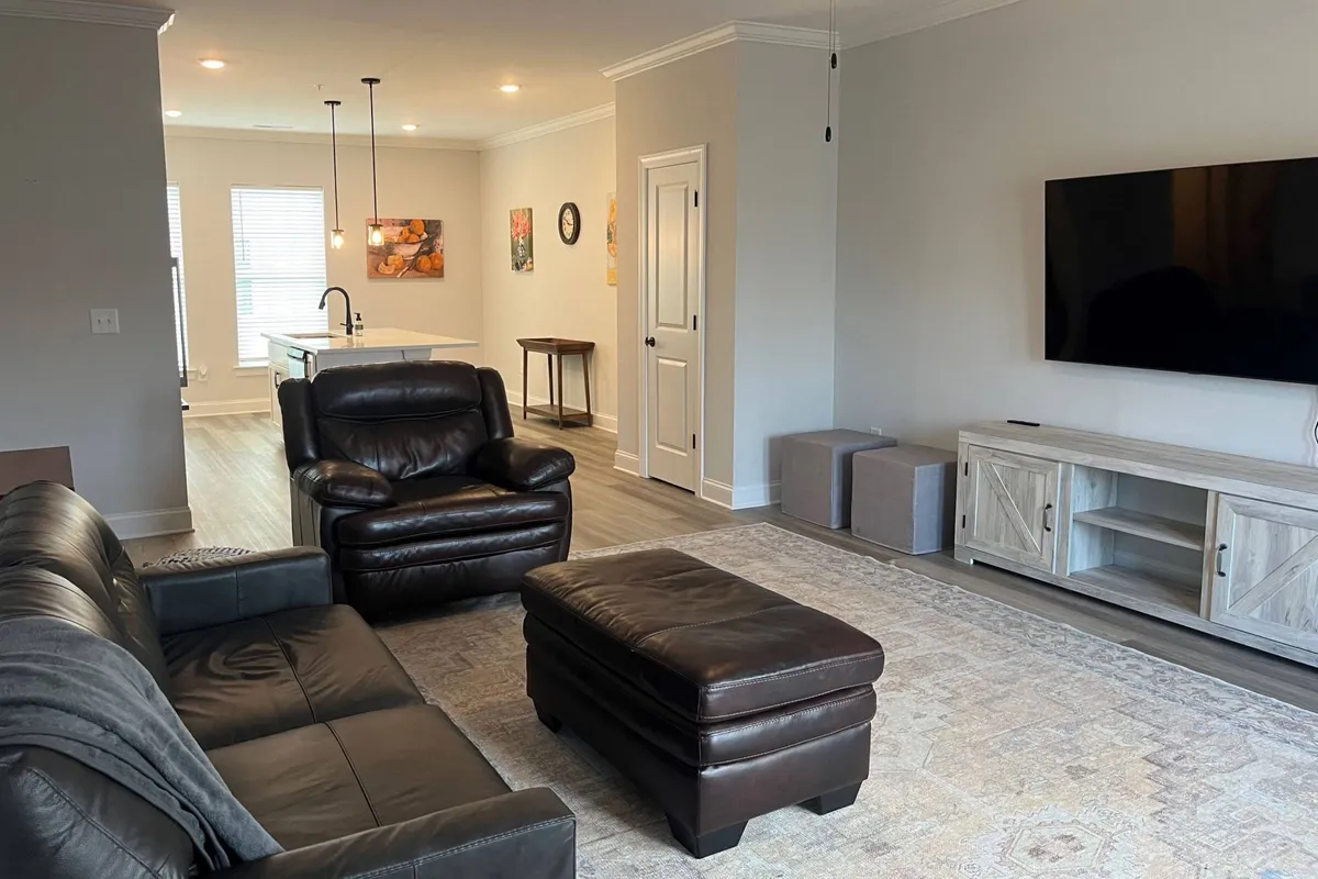 A cozy living space with a leather sofa, coffee table, television, and a dining area in the background. The setup encourages socializing, relaxing, and shared meals—all in a modern, welcoming atmosphere.