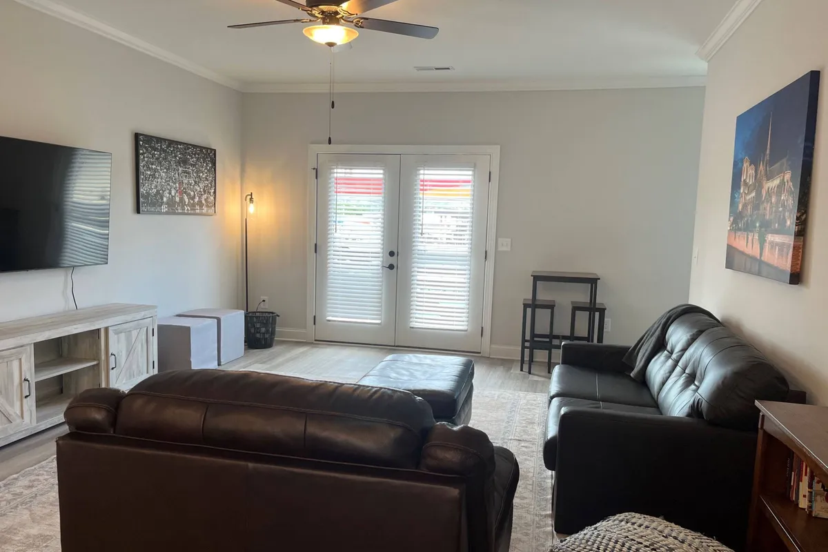 A comfortable living area featuring plush sofas, a television, double doors leading outside, and bright artwork. The inviting space is ideal for both relaxation and informal work sessions, with the double doors suggesting a seamless connection to outdoor spaces.
