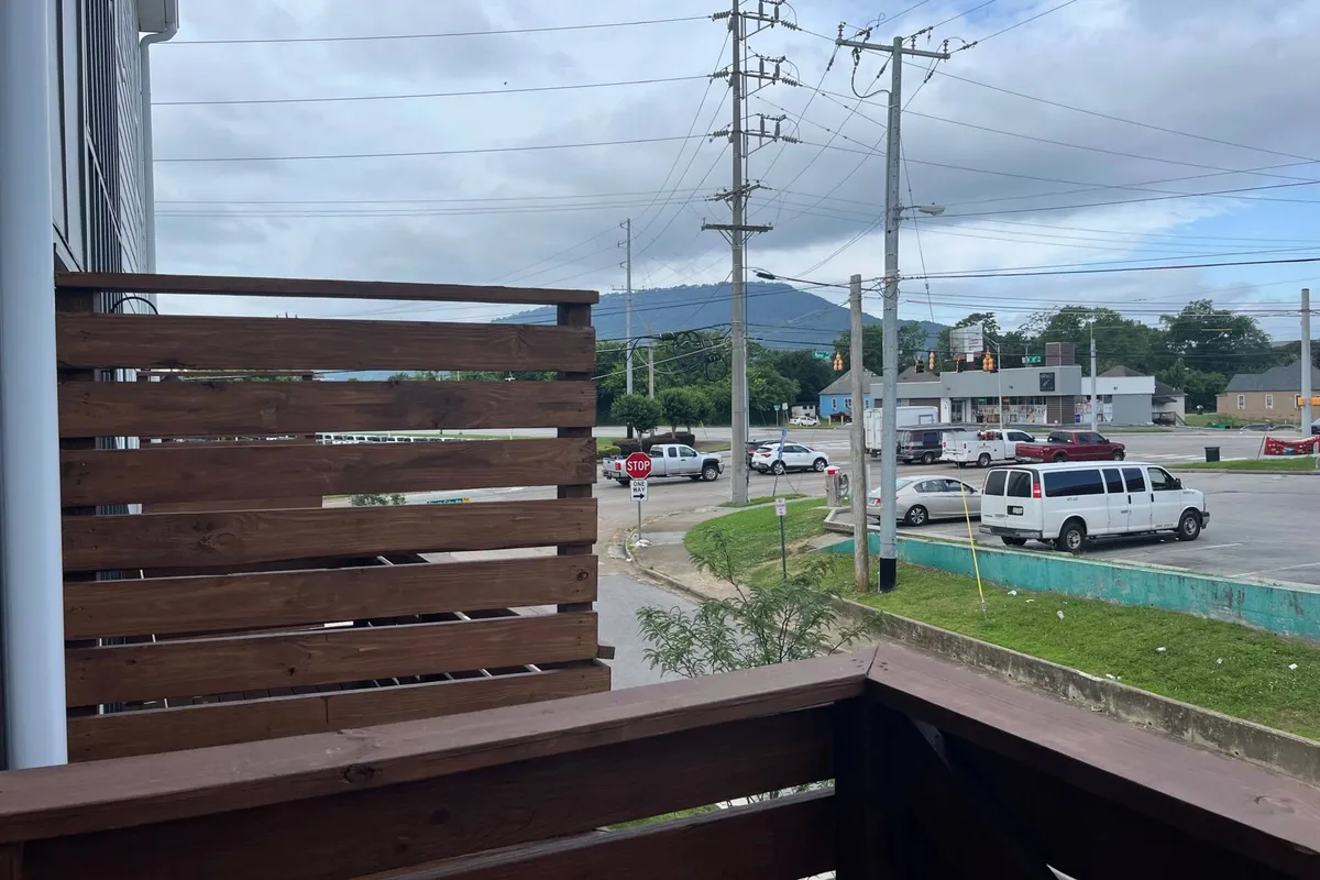 A private wooden balcony with distant mountain views, set above an urban street. The scene captures a calming spot for morning coffee or evening relaxation, blending city energy and natural tranquility.