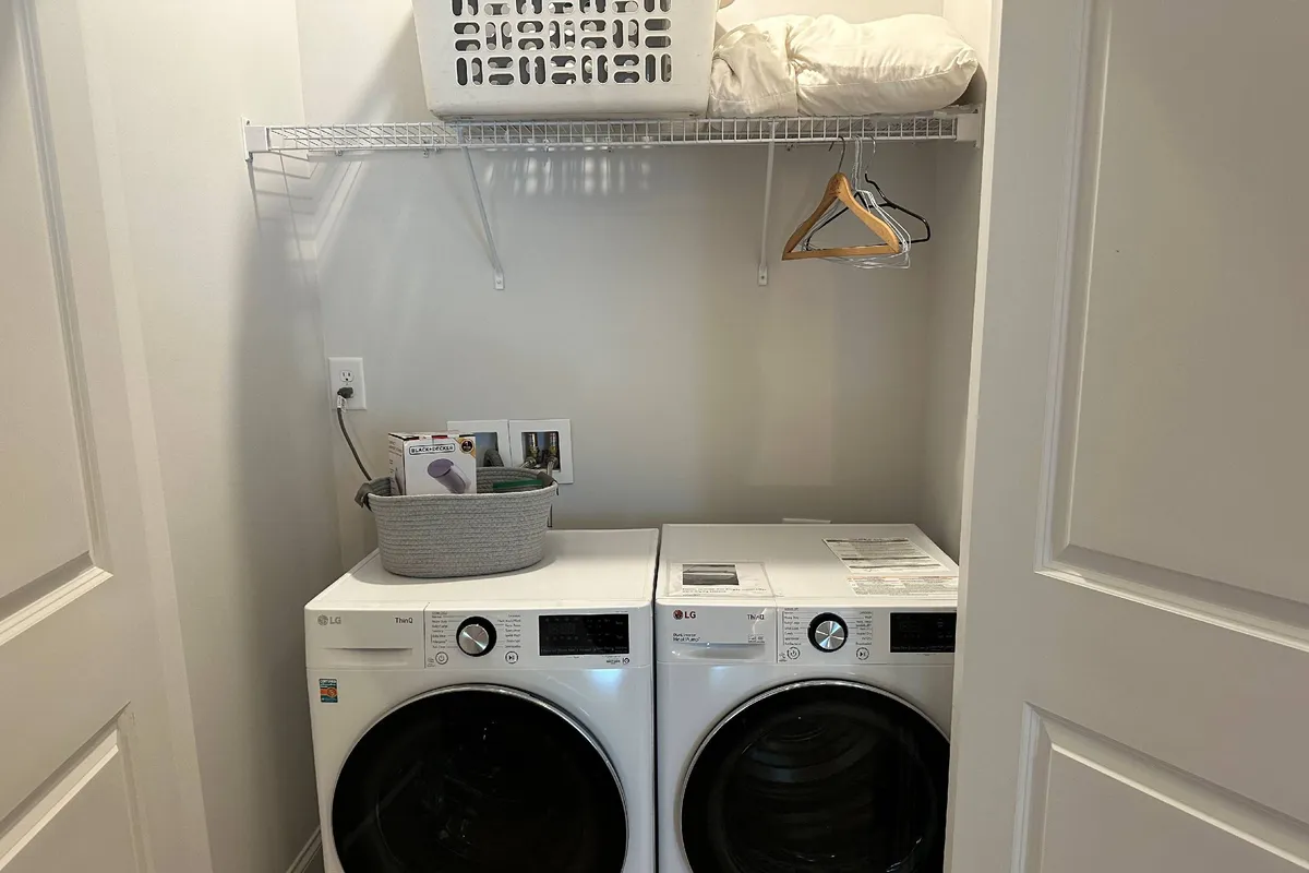 A tidy, well-organized laundry room featuring modern washer and dryer units, a shelf with a laundry basket, and hangers for clothes. The space feels practical and efficient, designed for ease of use.
